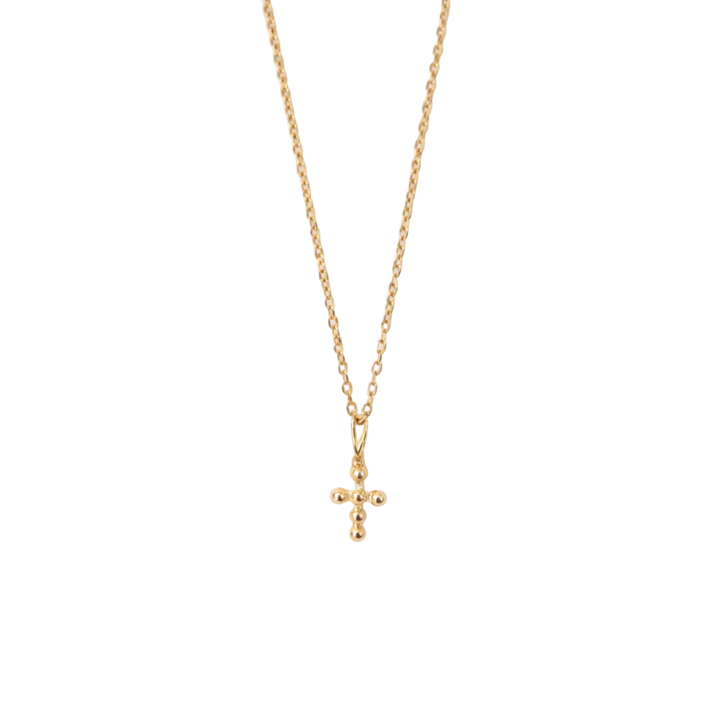 Gold necklace with a small cross pendant on a white textured background