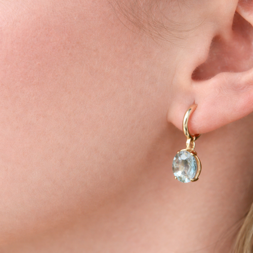 Close-up of an ear wearing a gold earring with a clear gemstone.